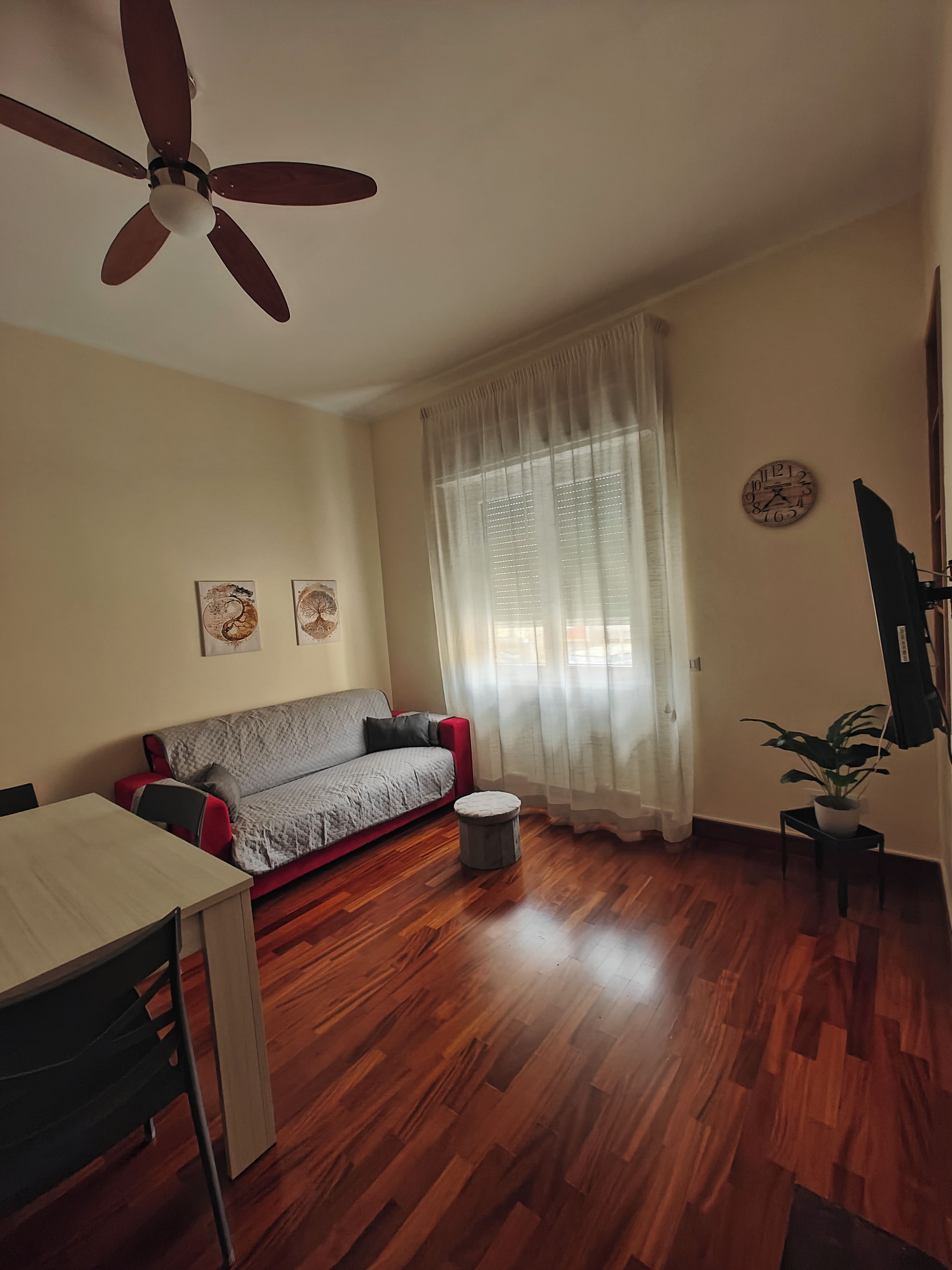 A living room with a ceiling fan, a sofa, a dining table, a small round table, and a potted plant.