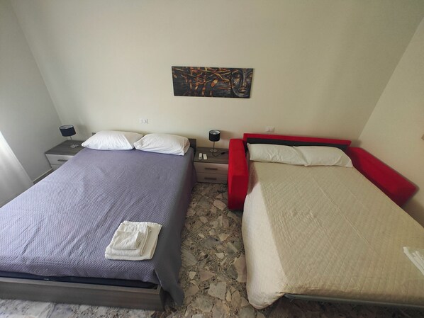 Habitació amb dos llits, cadascun amb un capçal d'un color diferent, una petita taula de nit amb una làmpada i un quadre a la paret.