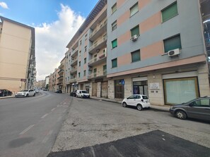 Un immeuble résidentiel à plusieurs étages, doté de balcons, d’un espace de stationnement et situé dans une rue où circulent des voitures.