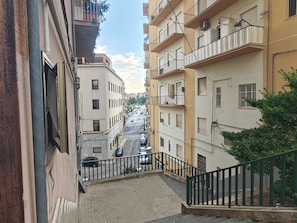 Une rue étroite, bordée de bâtiments des deux côtés, avec un chemin piétonnier et un escalier qui descend.