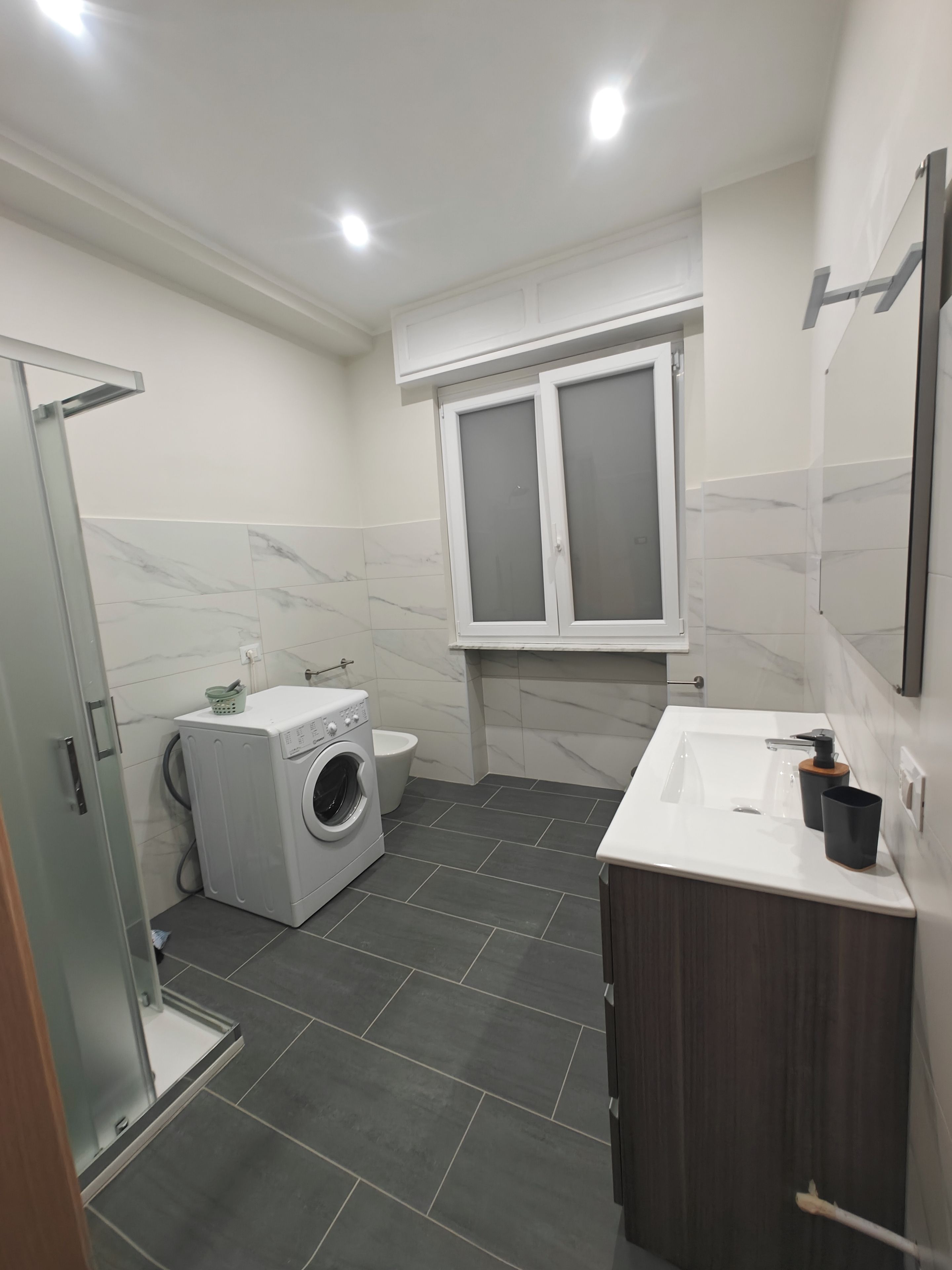 Een moderne badkamer met een douche, een wasmachine, een toilet en een wastafel.