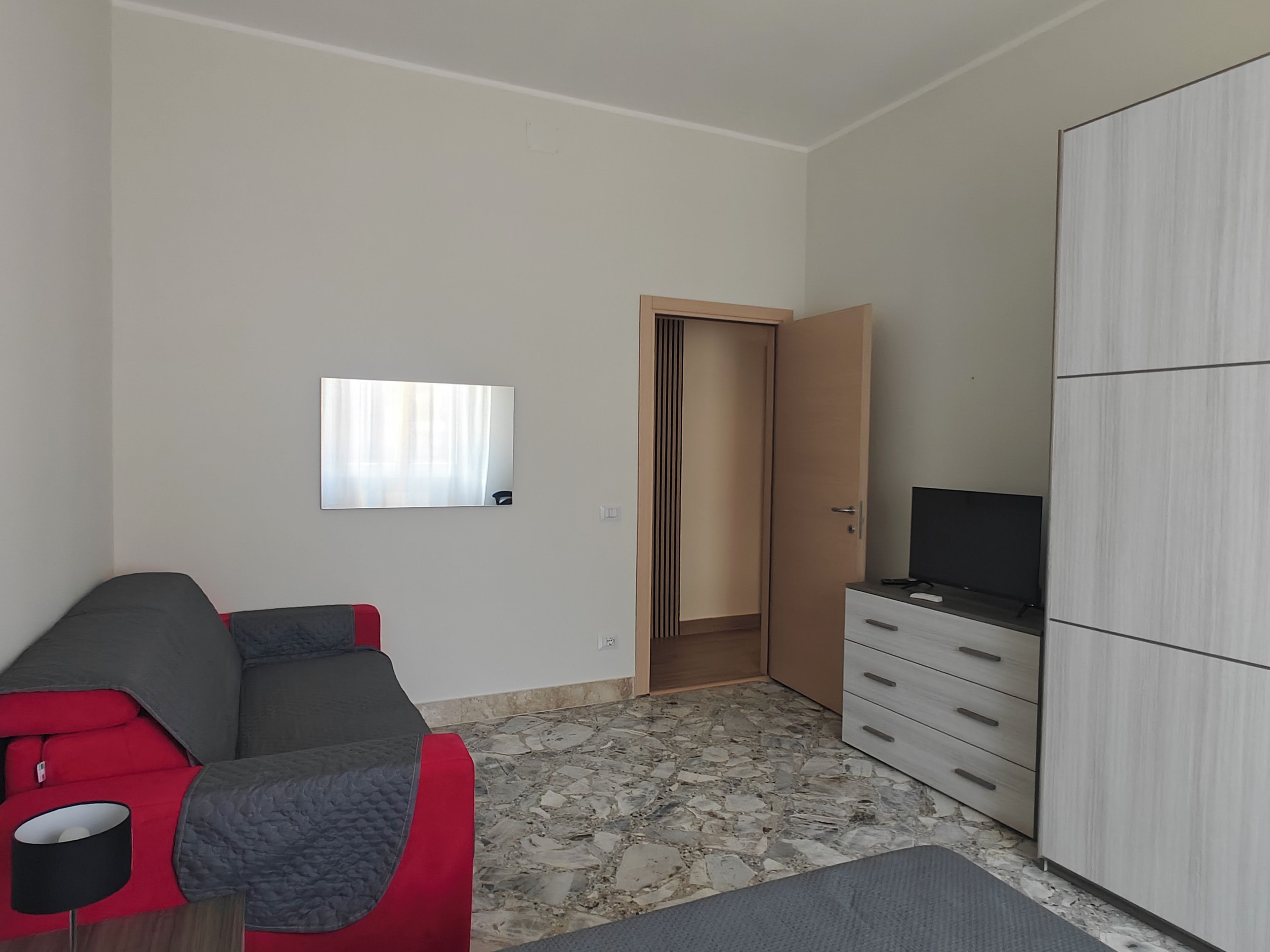 Una habitación con sofá, televisor en un mueble, armario y puerta que da a otra estancia.