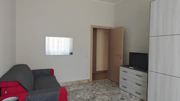 Una habitación con sofá, televisor en un mueble, armario y puerta que da a otra estancia.