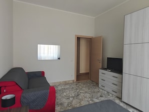 Habitació amb un sofà, una televisió sobre un moble, un armari i una porta que condueix a una altra habitació.
