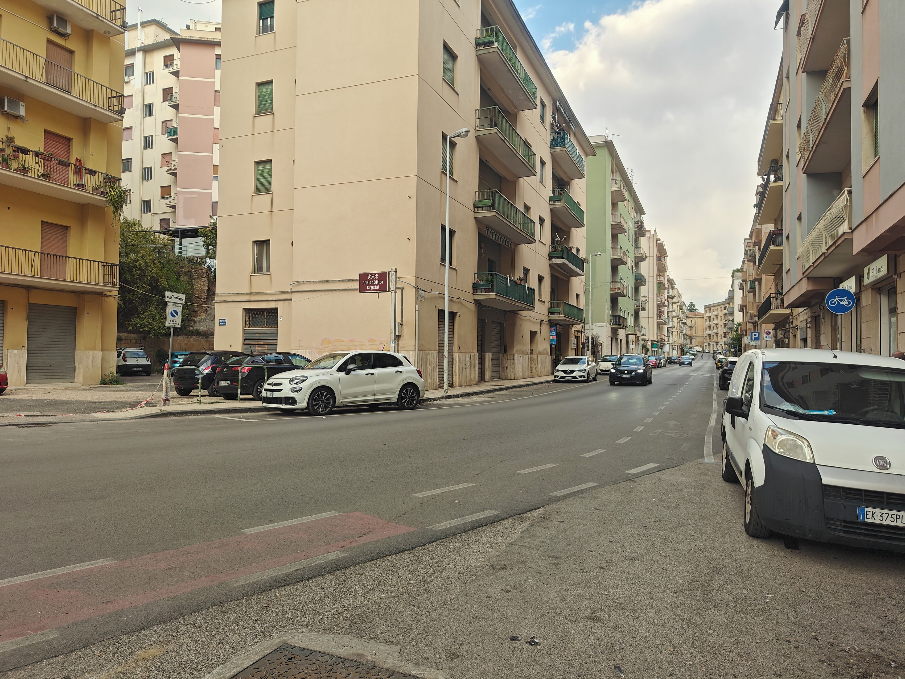 Eine Straße gesäumt von mehrstöckigen Wohnhäusern, parkenden Autos und wolkenlosem Himmel.