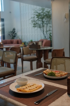 A dining table with a plate of food, a bowl, and cutlery.