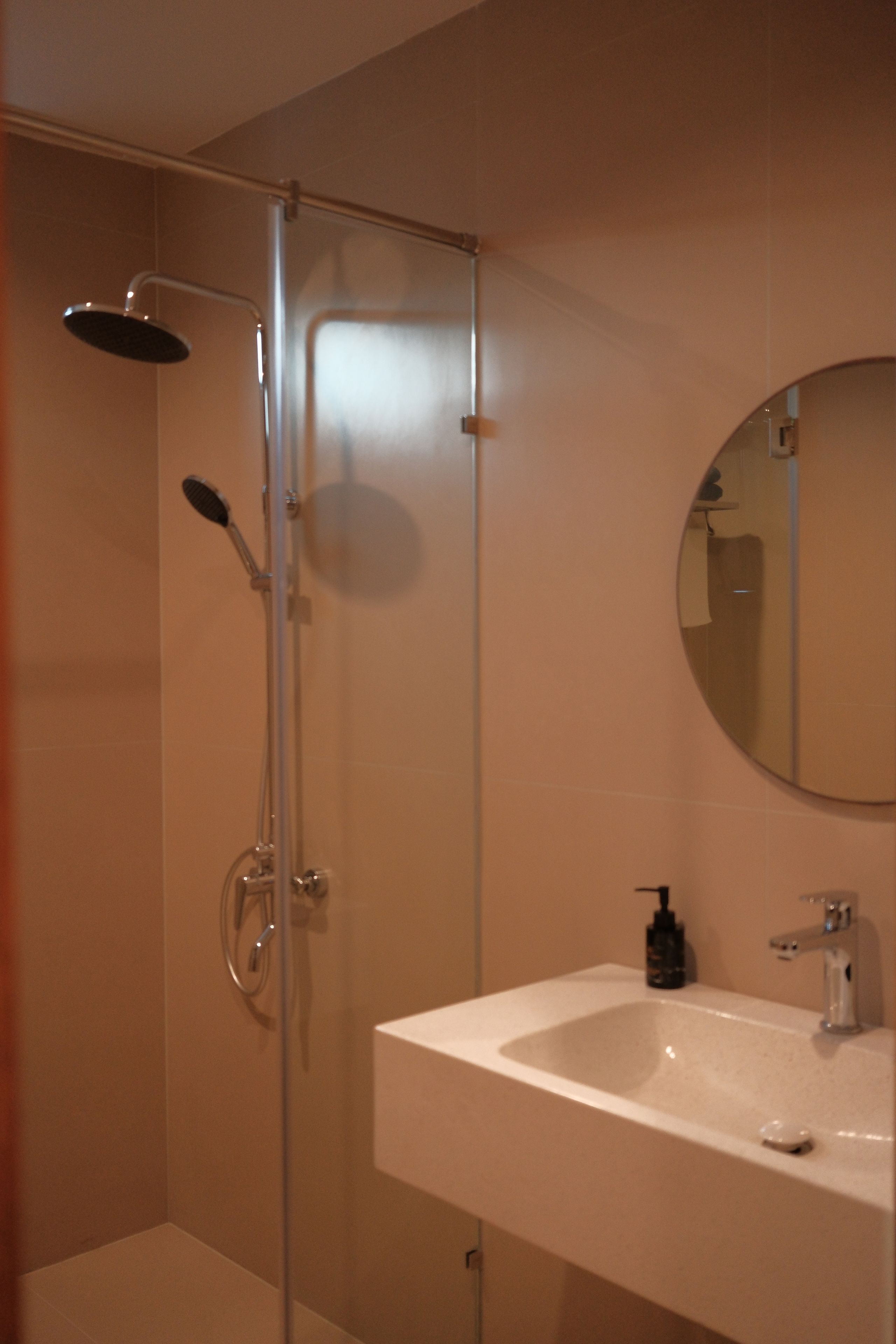 A bathroom with a glass-enclosed shower, a white sink, and a round mirror.