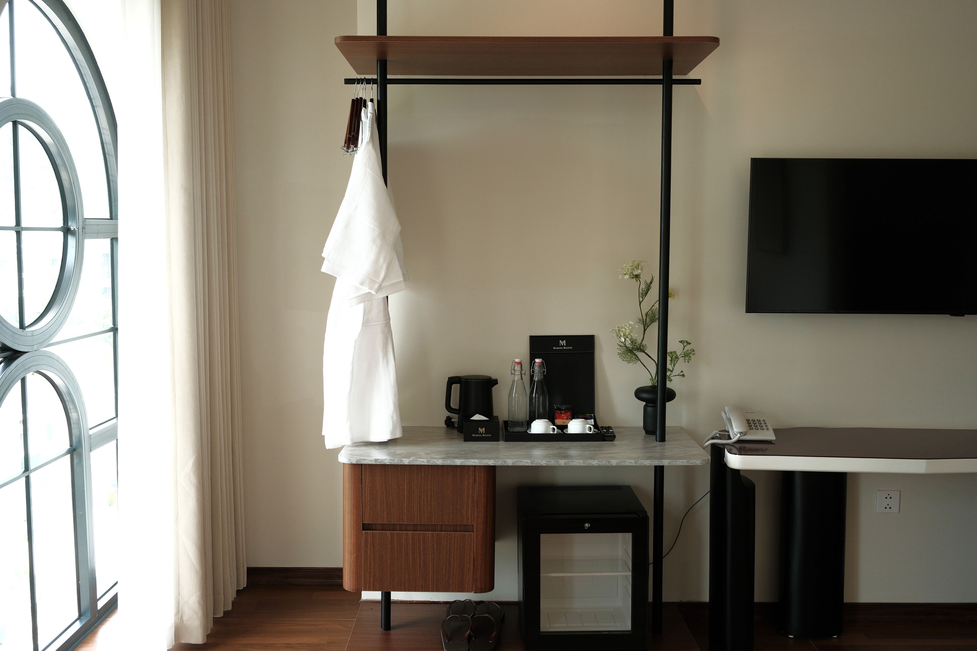 Ein Hotelzimmer mit einem Holztisch, einer Kaffeemaschine, einem kleinen Kühlschrank und einem an der Wand montierten Fernseher.