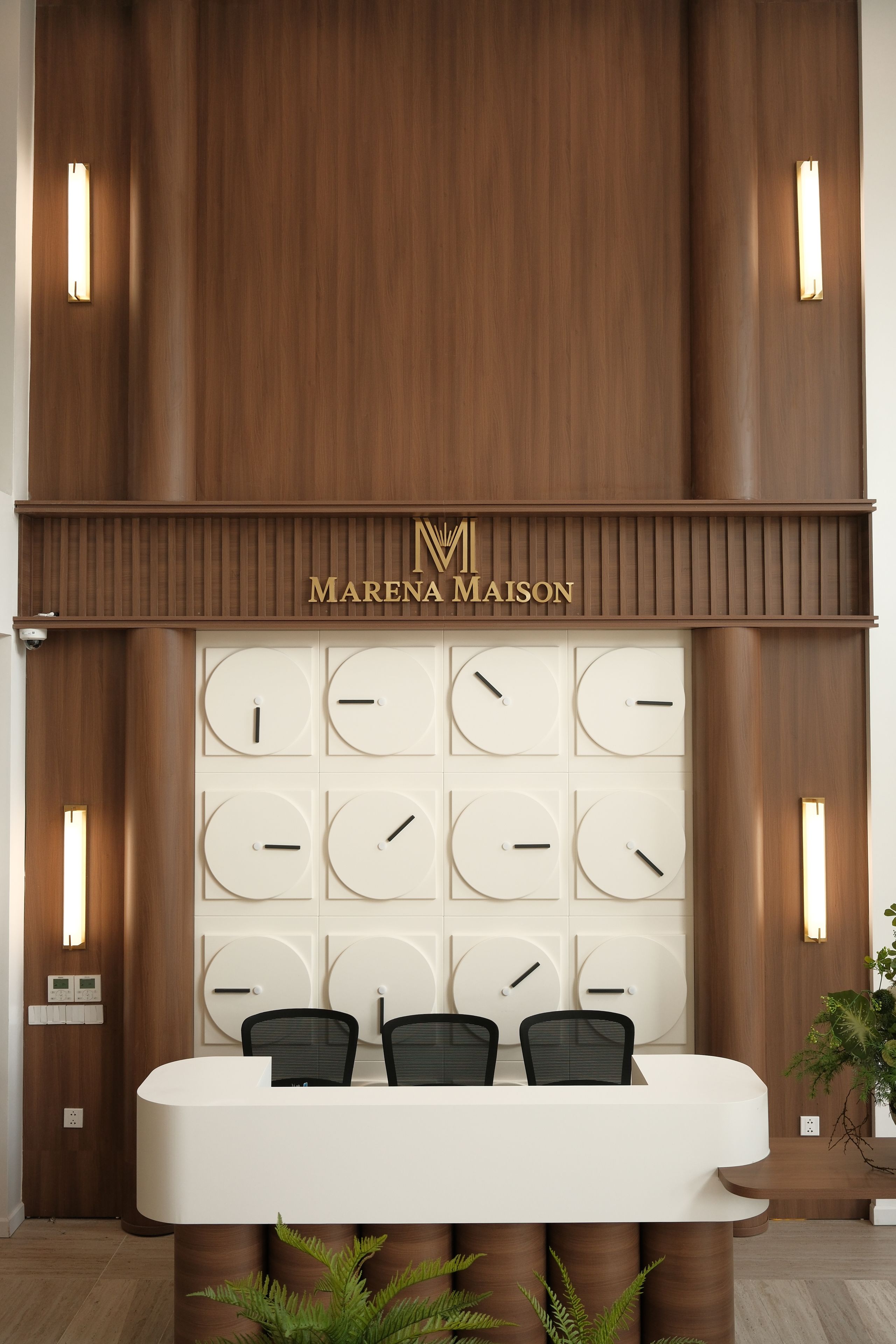 Een receptiebalie met een houten paneel als achtergrond, een klok en een bord met de tekst 'Marena Maison'.