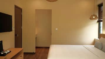A bedroom with a bed, a television on a stand, a wooden dresser, and a wicker ceiling light.