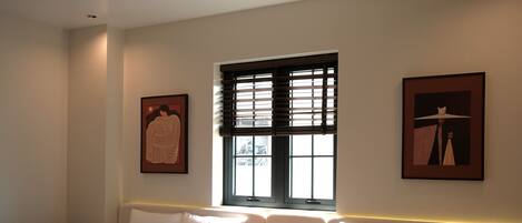 A hotel room with two beds, a window with blinds, and artwork on the walls.
