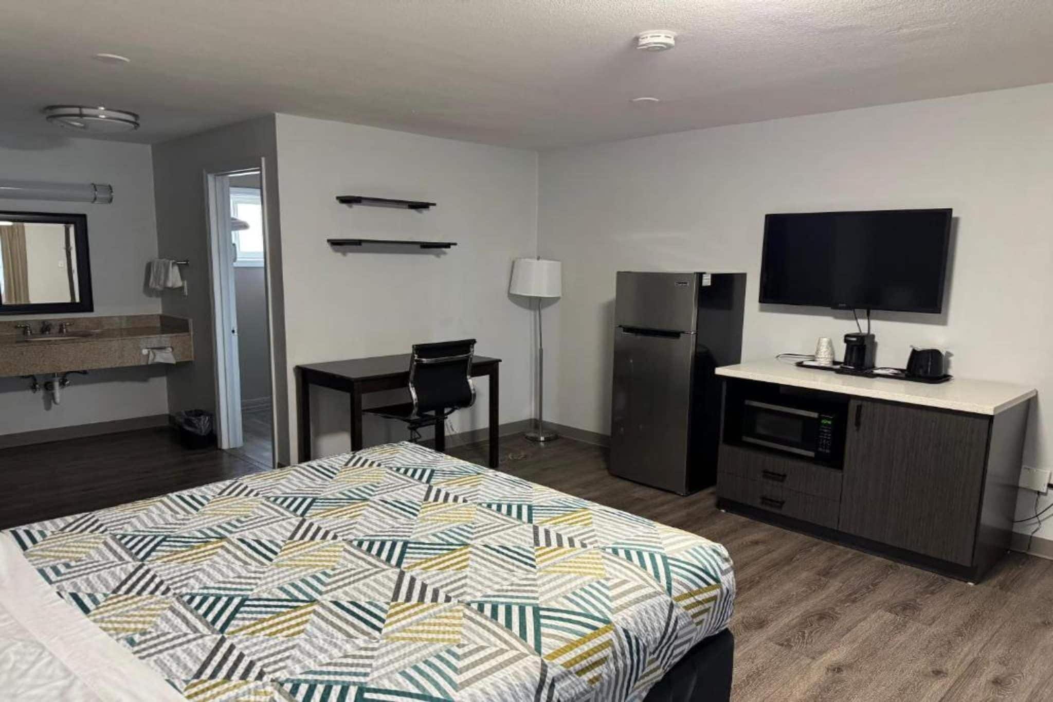 Quarto de hotel com cama, escrivaninha, frigorífico, televisão e casa de banho.