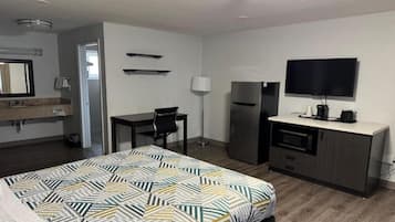 Quarto de hotel com cama, escrivaninha, frigorífico, televisão e casa de banho.