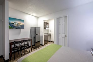 Habitació d'hotel petita amb un llit, una taula de treball amb cadires, un refrigerador, un microones i una porta que dona a un bany.