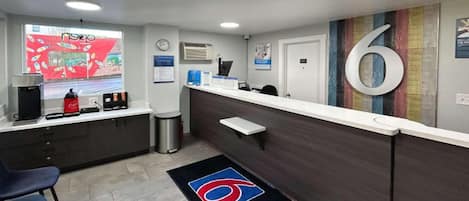 A reception area with a counter, chairs, a coffee machine, a trash bin, and a large number '6' on the wall.