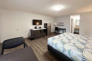 Habitació d'hotel amb llit, escriptori, cadira, televisió i petita cuina.