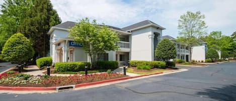 A modern hotel with a two-story structure, a covered entrance, and a landscaped front yard with a variety of plants.