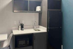 Una kitchenette compacta con microondas, cafetera y lavabo.