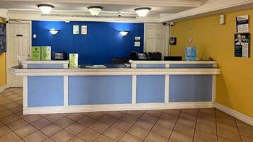 A reception desk with a blue and white color scheme, a tiled floor, and a yellow wall with informational posters.