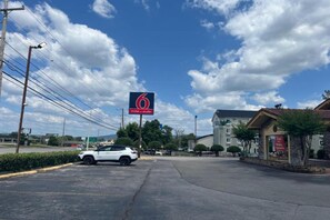 A parking lot with a white car, a motel sign, and a building with a red awning. - 1 King Bed | Smoking, Kitchen (Huntsville AL)