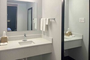 Un baño con un lavamanos blanco, un espejo y un perchero para toallas.