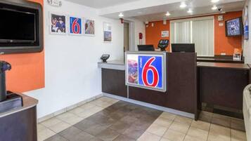 Zona de recepción de hotel con un cartel grande con el número '6', un televisor montado en la pared y una recepción con pantalla digital.
