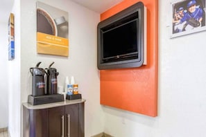 Quarto com estação de café, TV de tela plana presa em uma parede laranja e um quadro na parede.