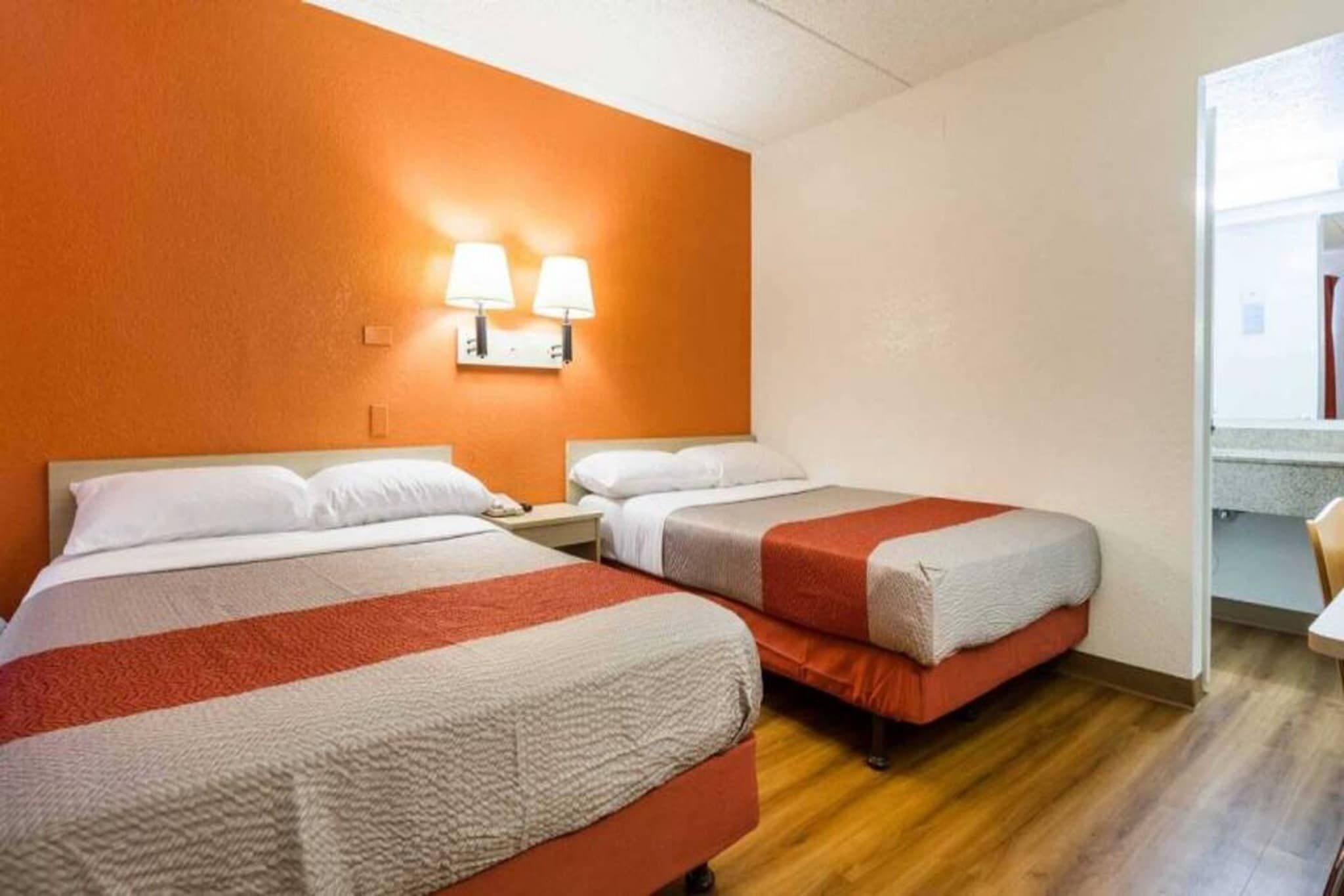 A hotel room with two beds, a wooden floor, and two wall-mounted lamps.
