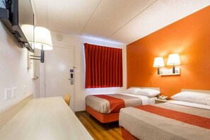 Habitación de hotel con dos camas, un escritorio, una ventana con cortinas rojas y lámparas fijadas a la pared.