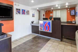 Zona de recepción de hotel con un cartel grande con el número '6', un televisor montado en la pared y una recepción con pantalla digital.