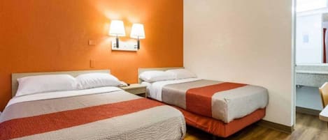 A hotel room with two beds, a wooden floor, and two wall-mounted lamps.