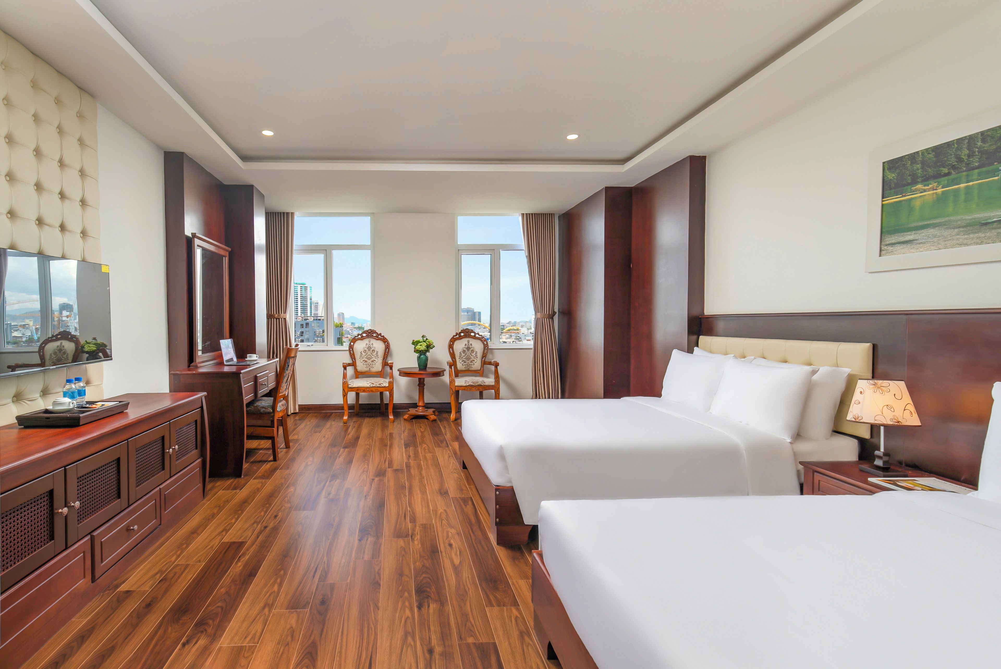 A hotel room with a bed, a desk with a chair, a TV, and a window with a view of buildings.