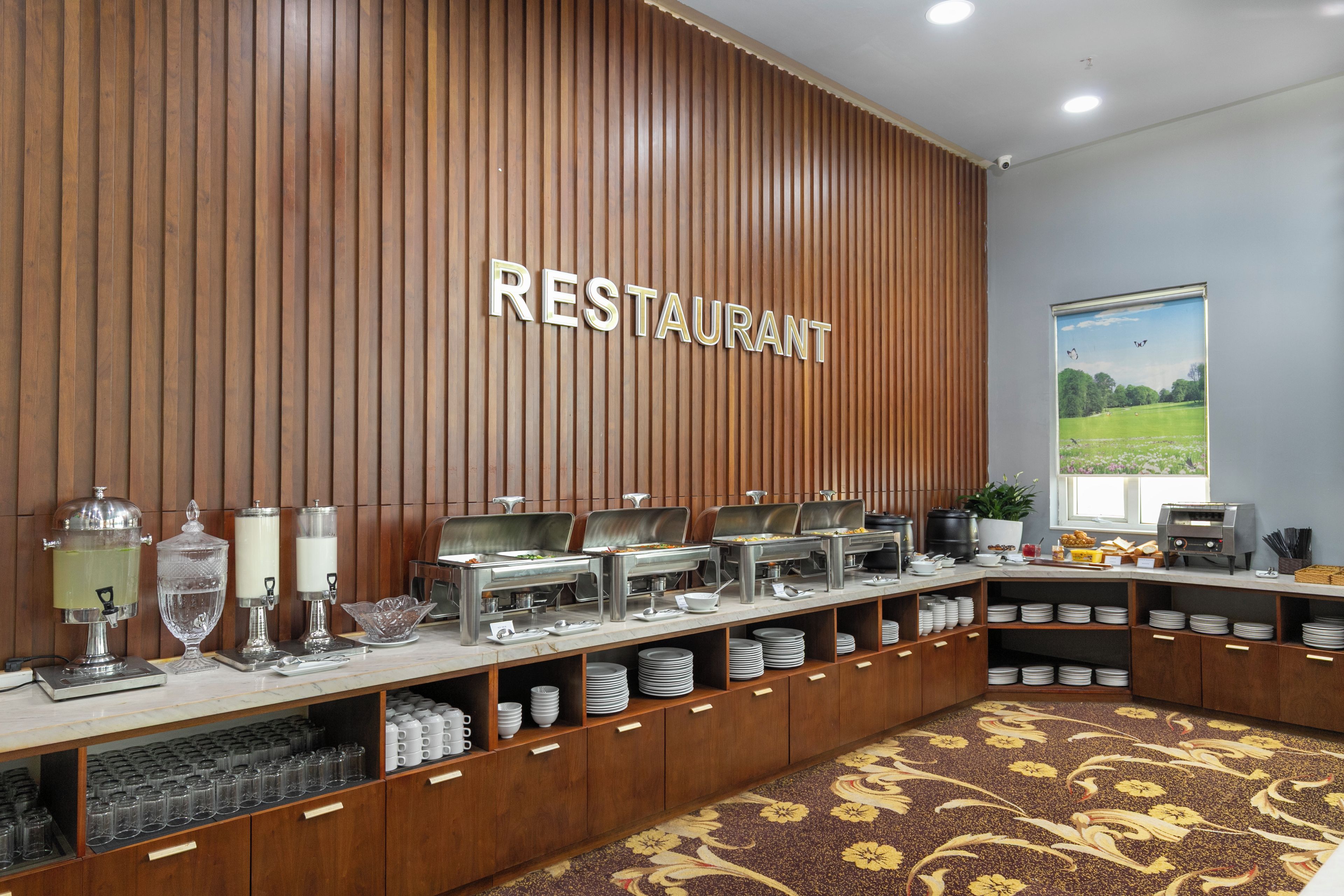 Ein Buffet mit mehreren Servierstationen, ein an der Wand befestigtes Schild mit der Aufschrift 'RESTAURANT' und ein Fenster mit Blick auf die Landschaft.