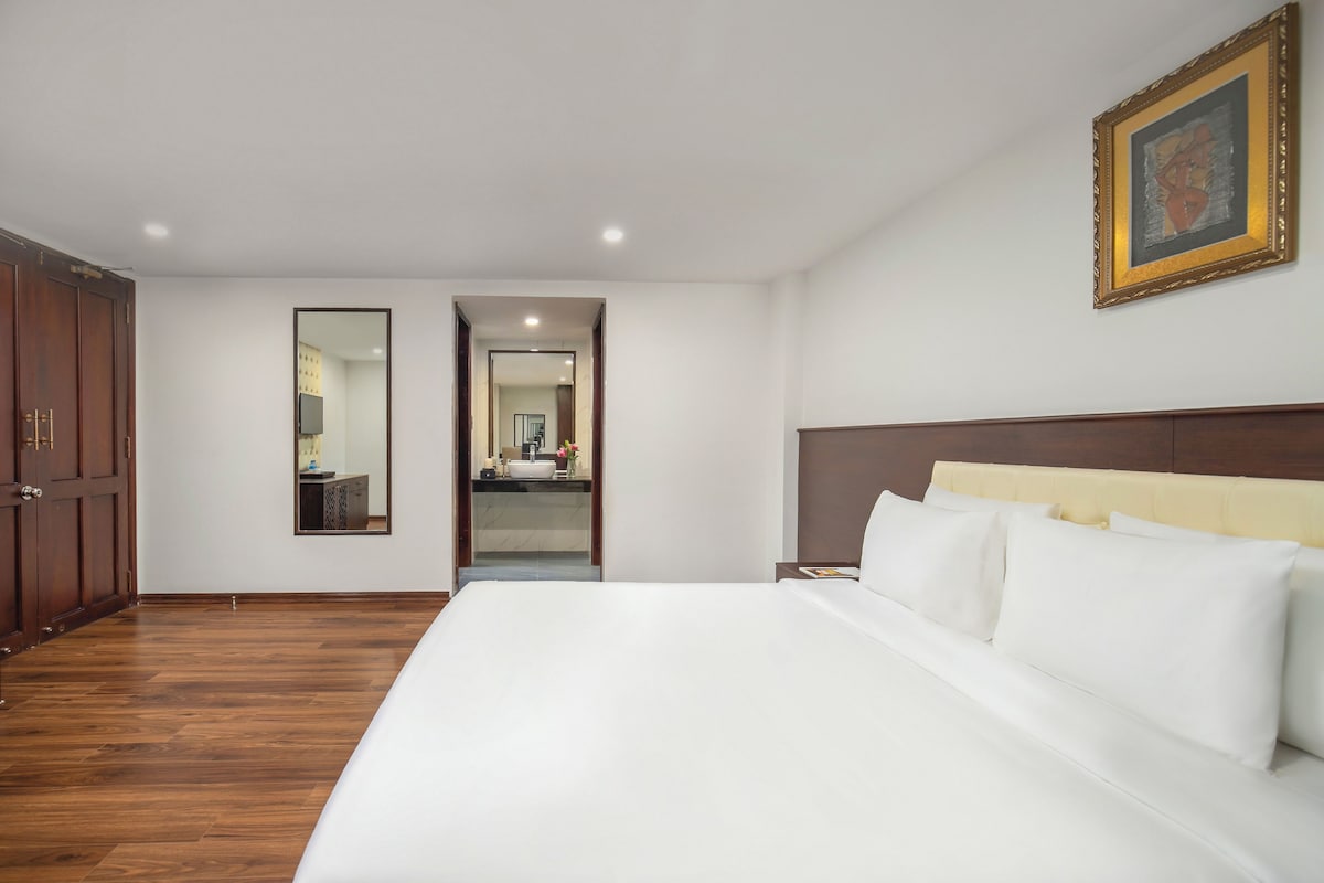Une chambre d’hôtel avec un grand lit, une armoire en bois, un miroir et une œuvre d’art encadrée accrochée au mur.