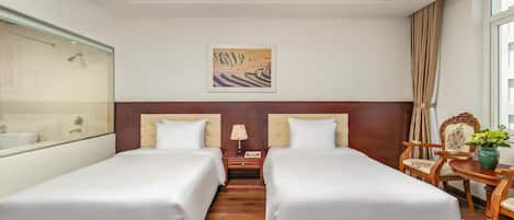 A hotel room with two beds, a nightstand, a lamp, a chair, and a window with curtains.