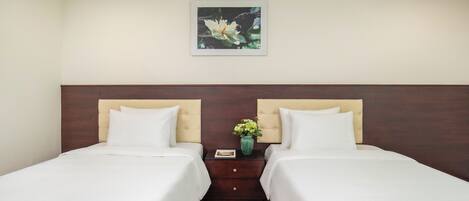 Quarto de hotel com duas camas, uma mesa de cabeceira com um vaso de flores e um quadro pendurado na parede.