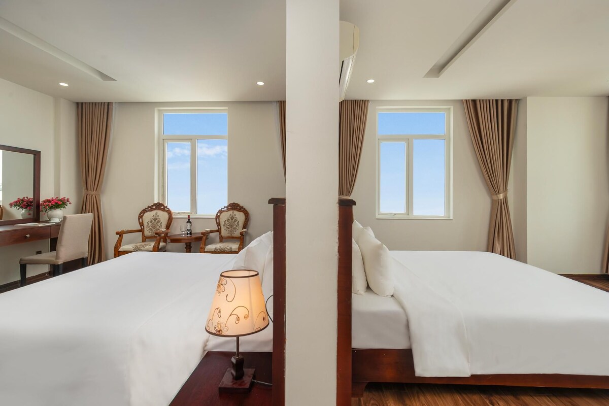 A hotel room with two beds, a desk with a chair, a lamp, and a window with curtains.