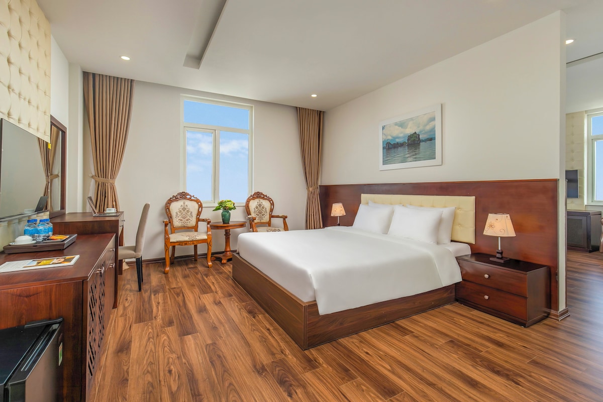 Une chambre d’hôtel avec un grand lit, un bureau avec une chaise, une petite table avec un vase et un tableau au mur.