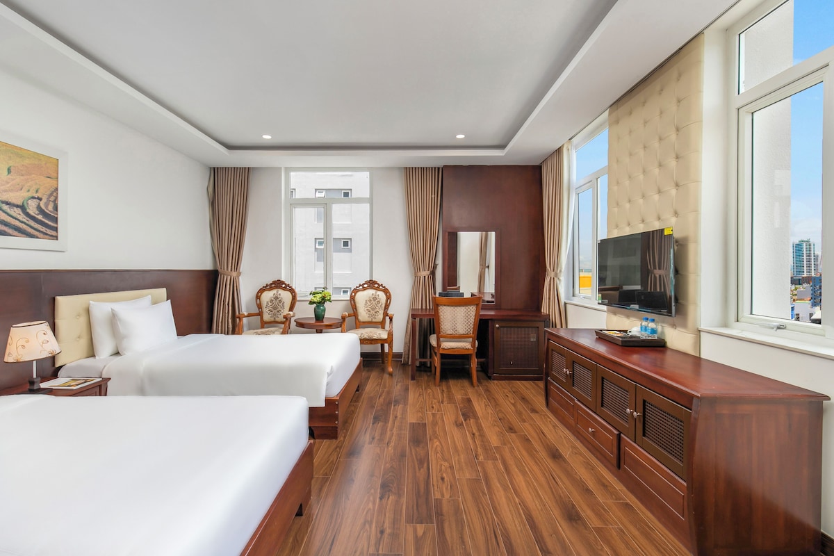 Une chambre d’hôtel avec deux lits, un bureau, une chaise, une télévision et une fenêtre donnant sur la ville.