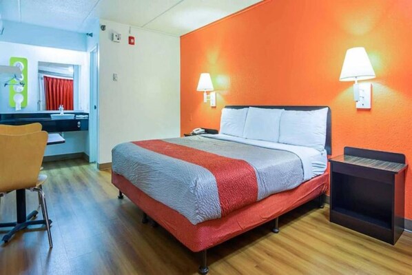 Een hotelkamer met een bed, een bureau, een stoel en een zichtbare badkamer door een open deur.