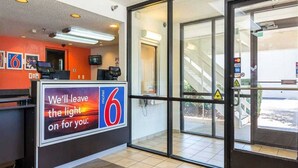 Ein Motel-Lobby mit einer Rezeption, einer großen beleuchteten '6' und einem Glastür-Eingang.