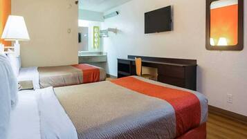 A hotel room with two beds, a desk, a chair, a TV, and a bathroom visible in the background.