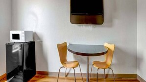 Ein Zimmer mit einem Flachbildfernseher an der Wand, einem kleinen Tisch mit zwei Stühlen und einem Kühlschrank mit integriertem Mikrowellenherd.