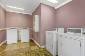 A laundry room with two front-loading washers and dryers, wooden flooring, and a white ceiling with recessed lighting.