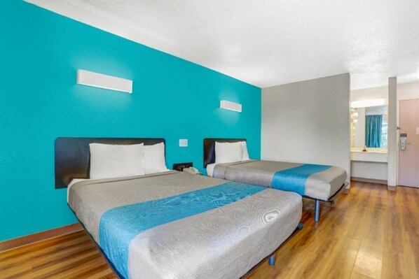 A hotel room with two beds, a wooden floor, and a bright turquoise wall.
