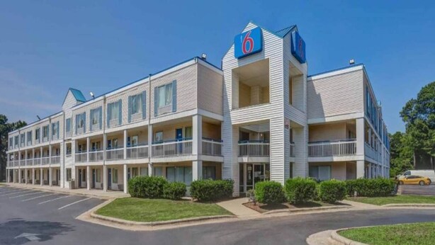 A motel with a central entrance, multiple balconies, and a parking lot. - 2 Full Beds | Smoking (Raleigh NC)