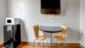 A room with a flat-screen TV mounted on the wall, a small table with two chairs, and a refrigerator with a microwave on top. - 2 Full Beds | Smoking (Raleigh NC)