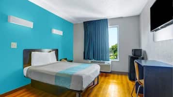 A hotel room with a bed, a desk, a television, and a window with curtains.
