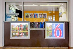 A hotel reception desk with a large number '6' sign, a framed quote, and a check-out sign indicating 11 AM. - 1 Queen Bed | Non-Smoking (Raleigh NC)