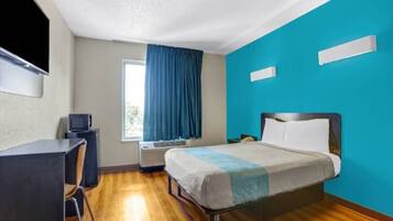 A hotel room with a bed, desk, and a television.